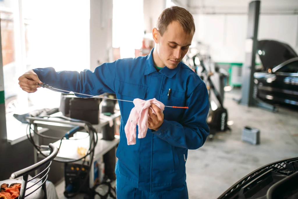 A service worker using an oil rod to check the oil levels in a car engine