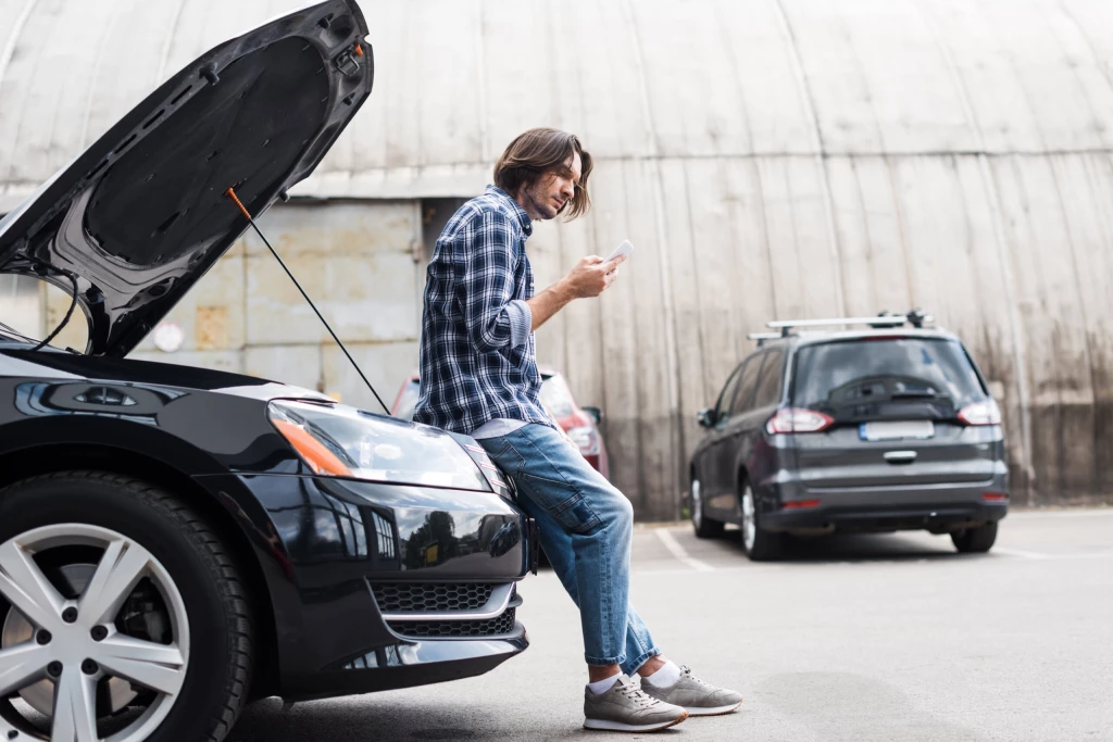 A man sitting on his car contacting roadside assistance