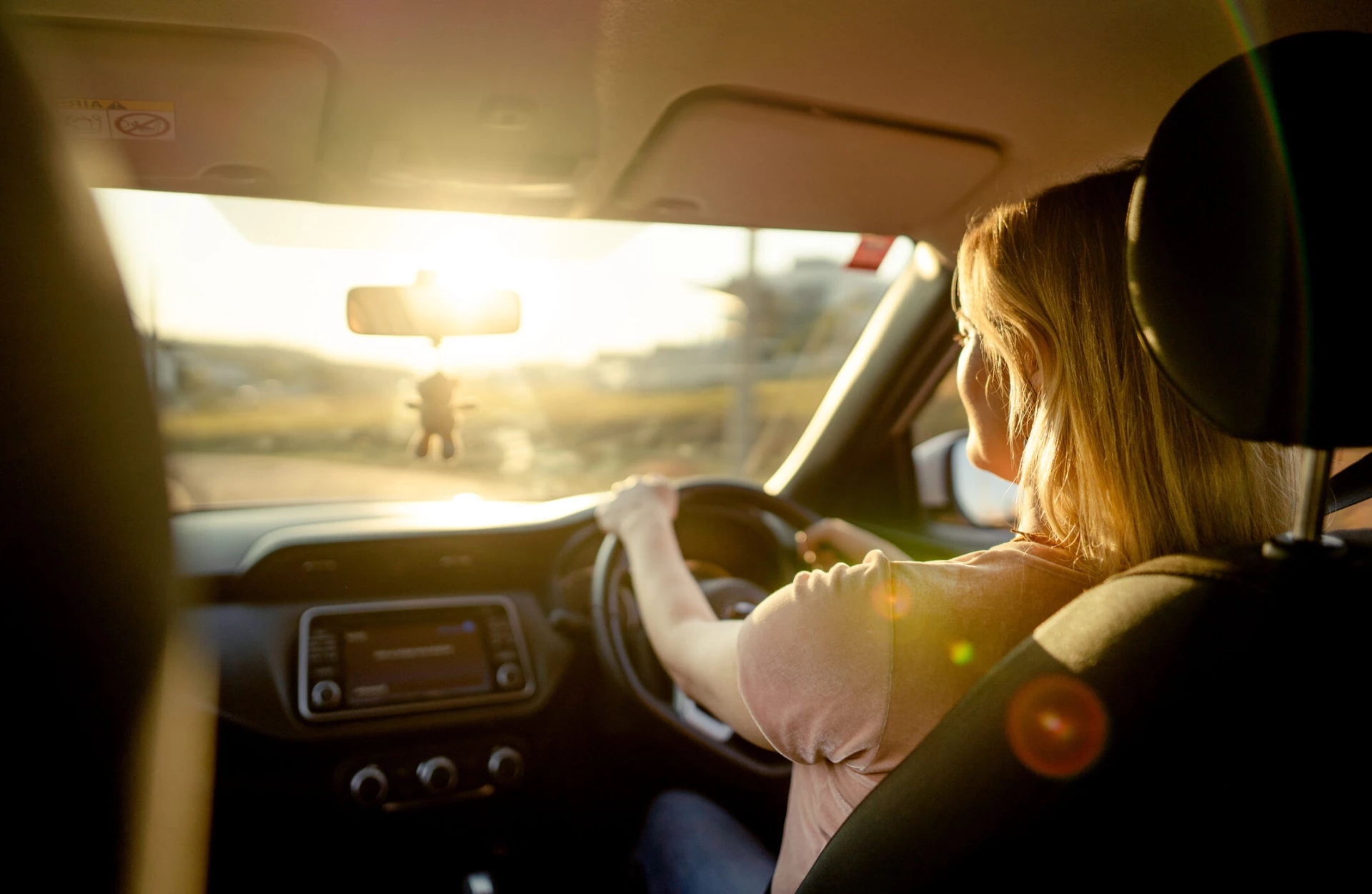 REAR VIEW OF A WOMAN DRIVING HER CAR ALONG A ROAD